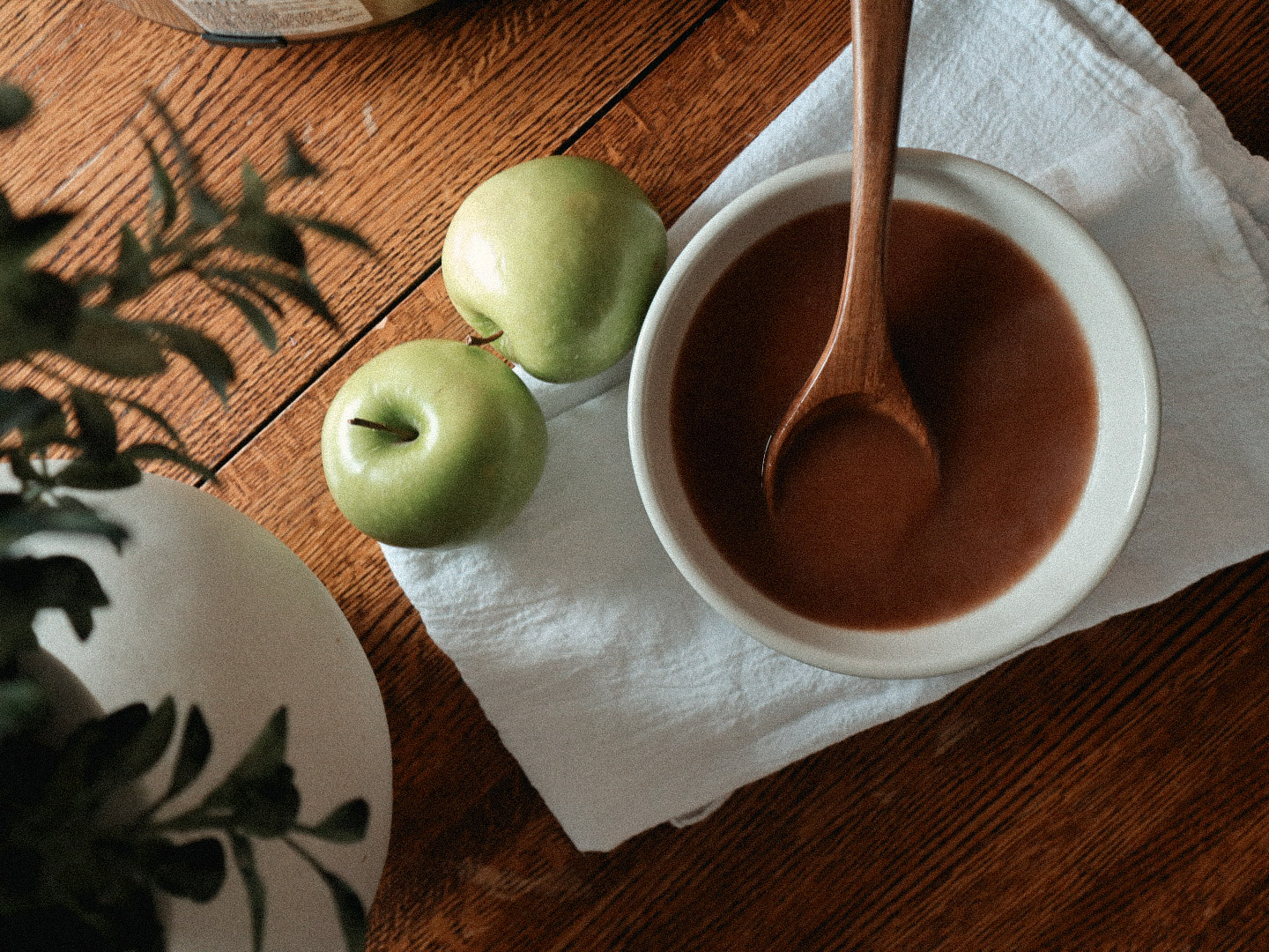 A bowl of soup and apples on a wooden table